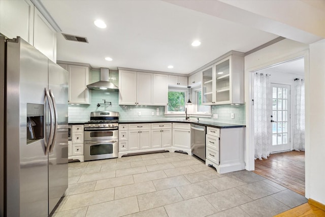 1219 Candlelight Ln, Houston, TX 77018 - kitchen with appliances with stainless steel finishes, wall chimney range hood, dark countertops, tasteful backsplash, and glass insert cabinets