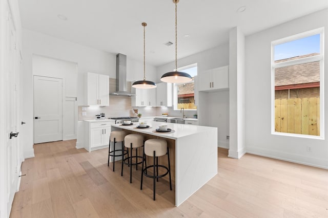 819 Dorothy St Unit B, Houston, TX 77008 - kitchen with wall chimney exhaust hood, light wood-style floors, a kitchen island, white cabinetry, and light countertops