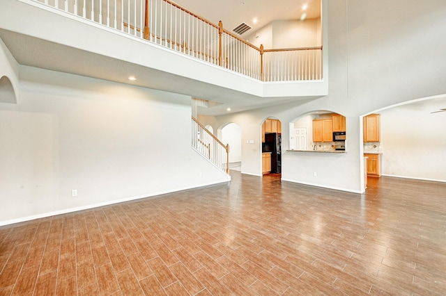 1752 Cypress Meadows Dr, Dickinson, TX 77539 - unfurnished living room with a towering ceiling, stairway, light wood-style flooring, arched walkways, and baseboards