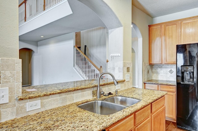 1752 Cypress Meadows Dr, Dickinson, TX 77539 - kitchen featuring black fridge with ice dispenser, a sink, arched walkways, light stone countertops, and backsplash