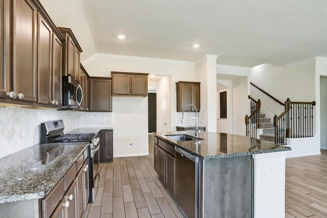 28618 Monarch Cliffs Dr, Fulshear, TX 77441 - kitchen featuring appliances with stainless steel finishes, a sink, light wood-style flooring, dark stone counters, and ornamental molding