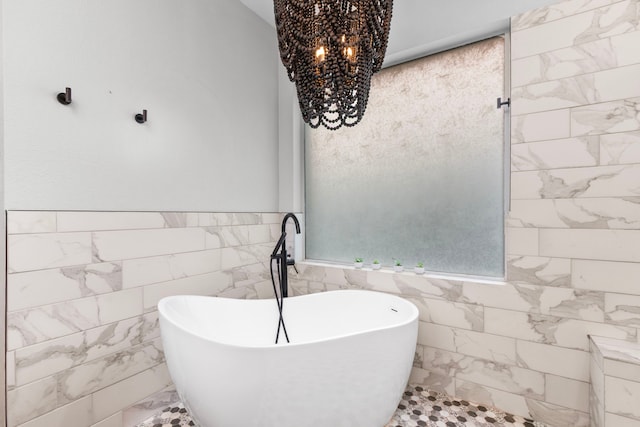 3815 Griffin Ln, Missouri City, TX 77459 - bathroom featuring tile walls, a freestanding tub, marble finish flooring, a chandelier, and a wainscoted wall