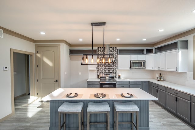 103 Whispering Oaks, Somerville, TX 77879 - kitchen featuring appliances with stainless steel finishes, gray cabinetry, wall chimney exhaust hood, decorative backsplash, and a breakfast bar area