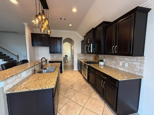 1216 Matthew Hills Ln, Spring, TX 77386 - kitchen with a sink, arched walkways, stainless steel microwave, light stone counters, and light tile patterned flooring