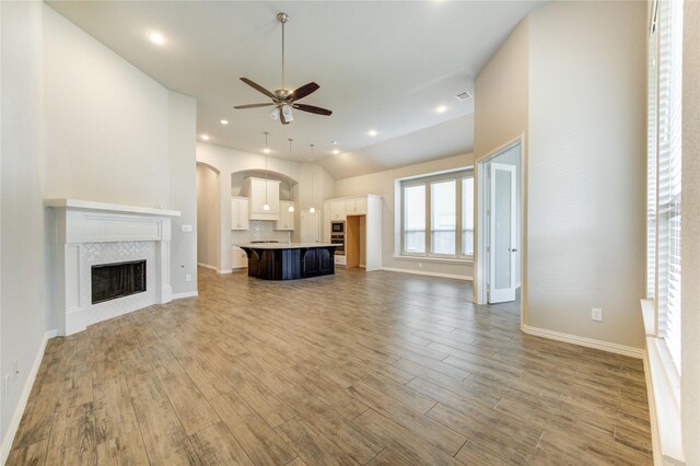 28418 Asher Falls Ln, Fulshear, TX 77441 - unfurnished living room featuring a ceiling fan, wood finished floors, a fireplace, arched walkways, and baseboards