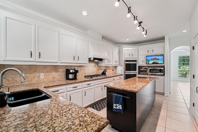 21885 Lost Mdw, New Caney, TX 77357 - kitchen featuring a sink, premium range hood, appliances with stainless steel finishes, arched walkways, and light tile patterned floors