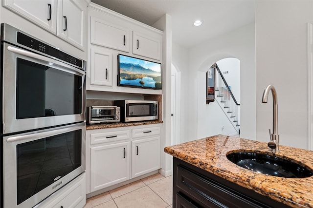 21885 Lost Mdw, New Caney, TX 77357 - kitchen featuring stainless steel appliances, a sink, light stone countertops, light tile patterned floors, and arched walkways