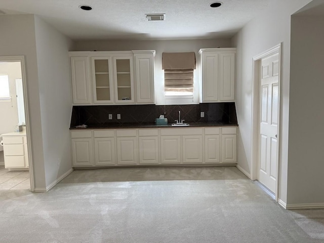 7222 Harmony Cv, Houston, TX 77036 - kitchen with light carpet, a sink, white cabinets, decorative backsplash, and glass insert cabinets