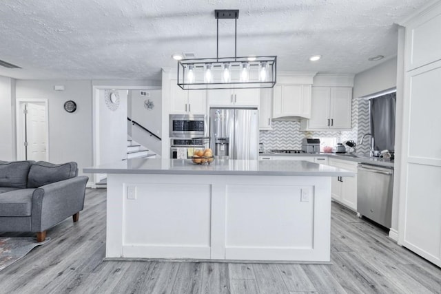 3031 Creek Manor Dr, Houston, TX 77339 - kitchen featuring appliances with stainless steel finishes, a textured ceiling, backsplash, white cabinets, and a kitchen island
