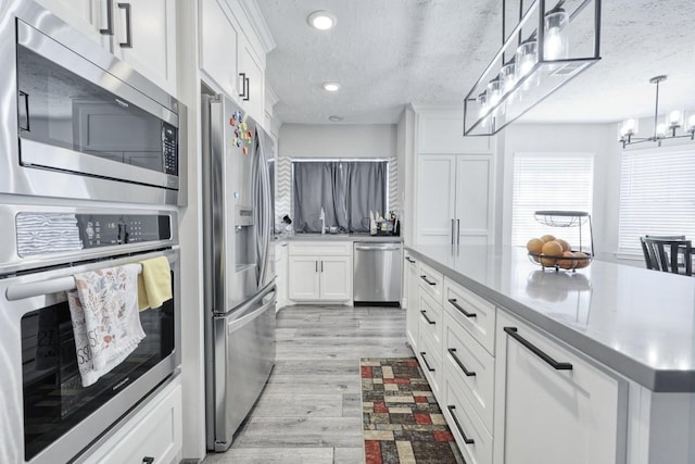 3031 Creek Manor Dr, Houston, TX 77339 - kitchen with stainless steel appliances, white cabinetry, light wood-style flooring, a textured ceiling, and a chandelier