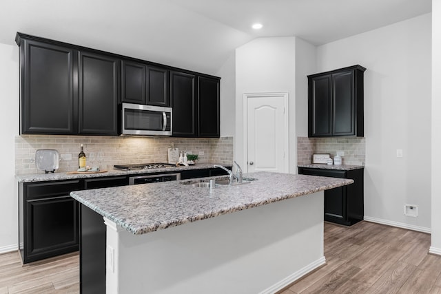 121 N Cadence Hills Loop, Conroe, TX 77318 - kitchen featuring appliances with stainless steel finishes, dark cabinets, light wood-style floors, backsplash, and vaulted ceiling