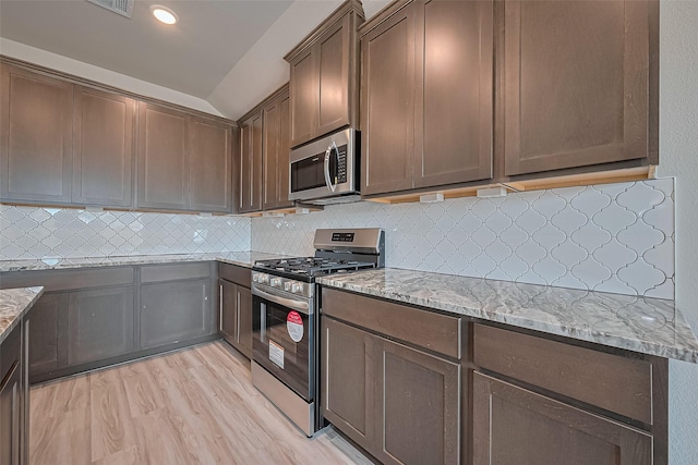 27227 Blue Pool Dr, Katy, TX 77493 - kitchen with stainless steel appliances, light stone counters, light wood-style flooring, decorative backsplash, and lofted ceiling