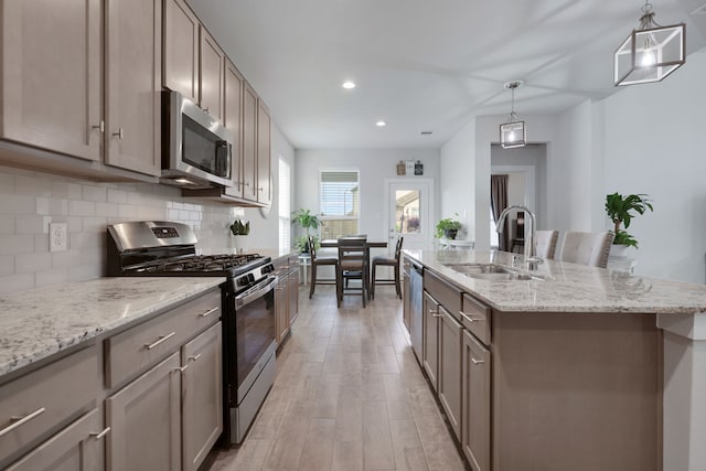 308 Spruce Oak Ln, Waller, TX 77484 - kitchen with stainless steel appliances, a sink, light wood-style flooring, decorative backsplash, and a center island with sink