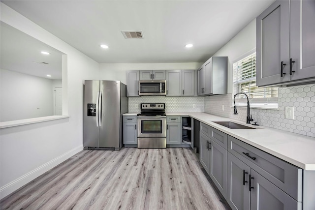 5751 Belmark St, Houston, TX 77033 - kitchen featuring stainless steel appliances, gray cabinets, a sink, light wood finished floors, and recessed lighting