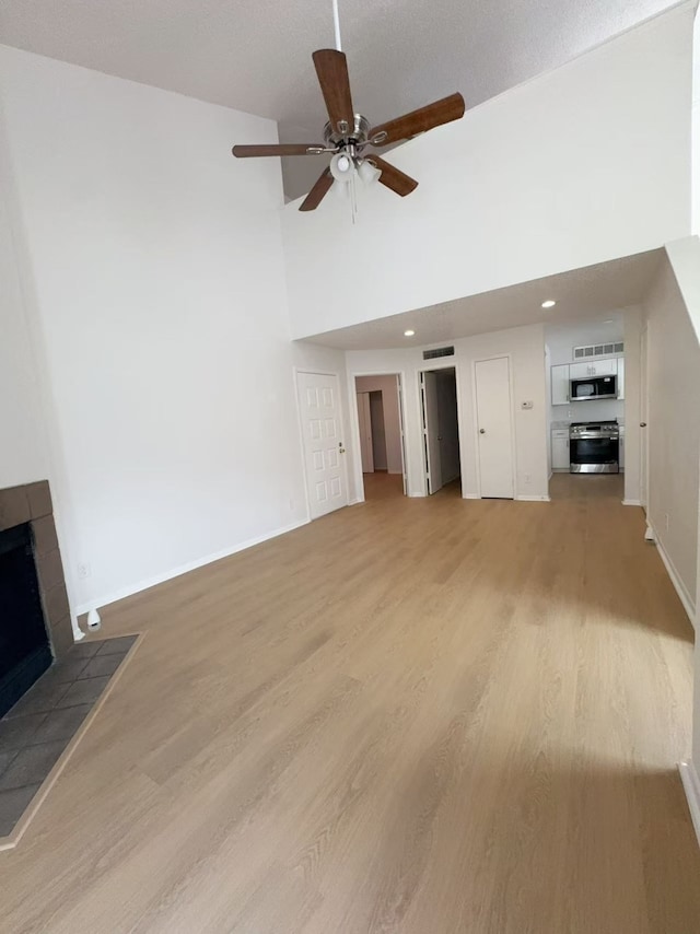 10855 Meadowglen Ln Unit 1121, Houston, TX 77042 - unfurnished living room with a tiled fireplace, high vaulted ceiling, a ceiling fan, light wood-type flooring, and baseboards