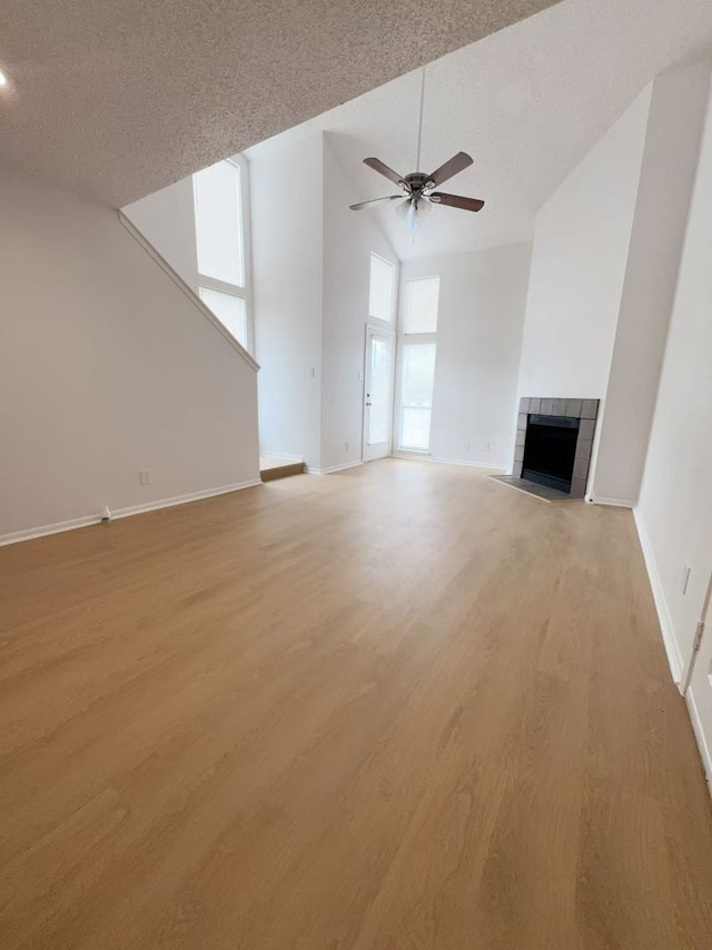 10855 Meadowglen Ln Unit 1121, Houston, TX 77042 - unfurnished living room featuring a ceiling fan, a tiled fireplace, light wood finished floors, baseboards, and high vaulted ceiling