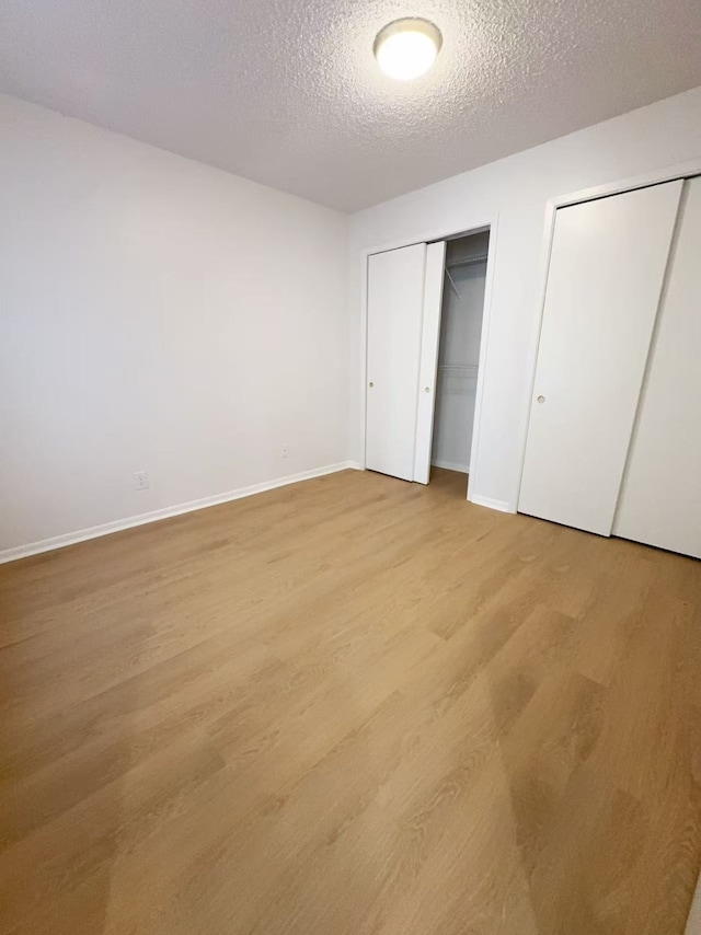10855 Meadowglen Ln Unit 1121, Houston, TX 77042 - unfurnished bedroom featuring multiple closets, light wood-type flooring, a textured ceiling, and baseboards