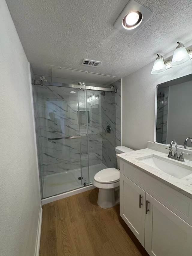 10855 Meadowglen Ln Unit 1121, Houston, TX 77042 - bathroom featuring wood finished floors, a marble finish shower, vanity, toilet, and a textured ceiling