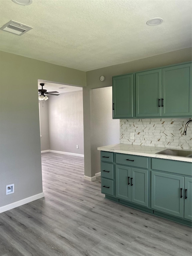 8630 Flossie Mae St, Houston, TX 77029 - kitchen with green cabinets, a sink, light wood-style flooring, tasteful backsplash, and a ceiling fan