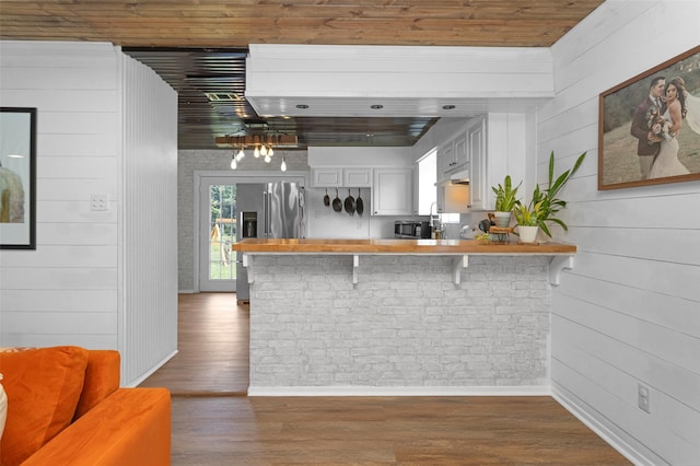 1137 Jones Rd, New Waverly, TX 77358 - kitchen featuring baseboards, a peninsula, wood walls, a breakfast bar area, and wood finished floors