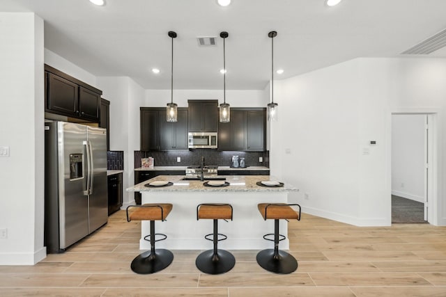 21517 Witham Promenade Ln, Magnolia, TX 77355 - kitchen with appliances with stainless steel finishes, light wood finished floors, a sink, a breakfast bar, and decorative backsplash