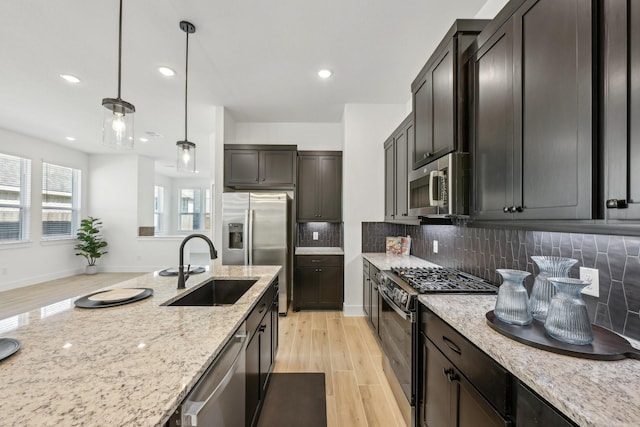 21517 Witham Promenade Ln, Magnolia, TX 77355 - kitchen featuring appliances with stainless steel finishes, a sink, light wood-style floors, light stone countertops, and decorative backsplash