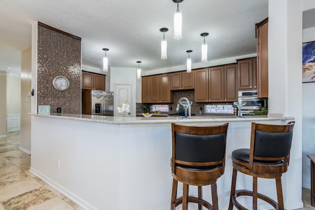 9802 Willowbridge Park Blvd, Houston, TX 77064 - kitchen featuring appliances with stainless steel finishes, decorative backsplash, a peninsula, light stone countertops, and pendant lighting