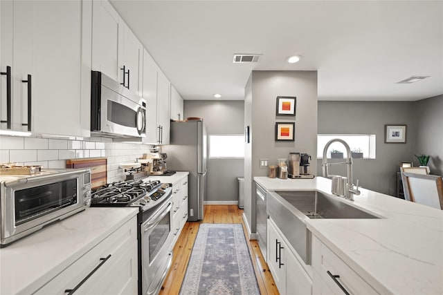 1716 W Dallas St Unit 11, Houston, TX 77019 - kitchen featuring appliances with stainless steel finishes, light wood finished floors, white cabinetry, decorative backsplash, and light stone countertops