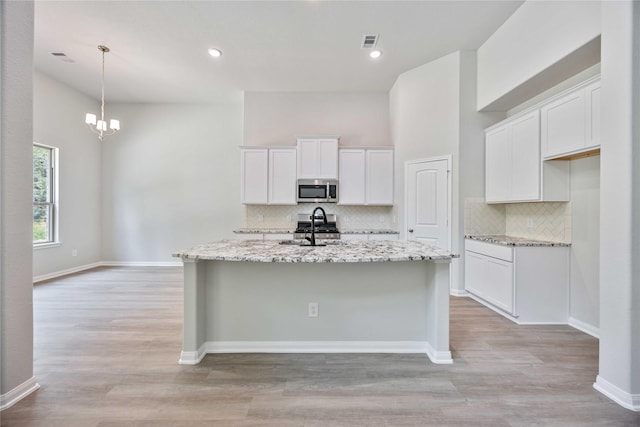1497 Rd 66114, Dayton, TX 77535 - kitchen with stainless steel microwave, decorative backsplash, an island with sink, white cabinetry, and light stone countertops