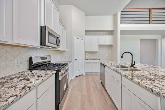 1497 Rd 66114, Dayton, TX 77535 - kitchen with appliances with stainless steel finishes, light wood-style floors, white cabinetry, decorative backsplash, and light stone counters