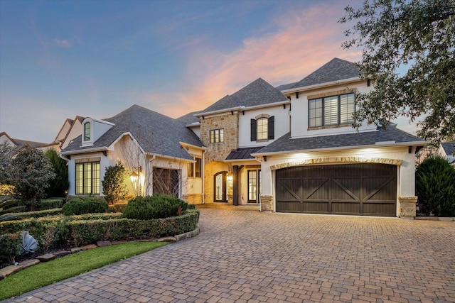 10 Broadwater Ct, Shenandoah, TX 77381 - french country style house with stucco siding, a garage, decorative driveway, roof with shingles, and stone siding