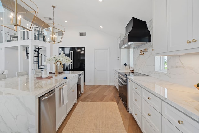 102 Lanai St, Tiki Island, TX 77554 - kitchen with wall chimney range hood, stainless steel appliances, a chandelier, backsplash, and light wood-style floors