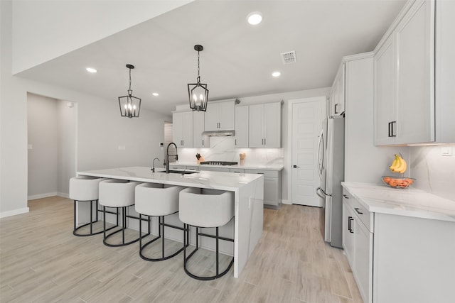 5107 Shimmering Brook Ln, Fulshear, TX 77441 - kitchen with freestanding refrigerator, a sink, gas cooktop, a breakfast bar area, and light wood-style flooring