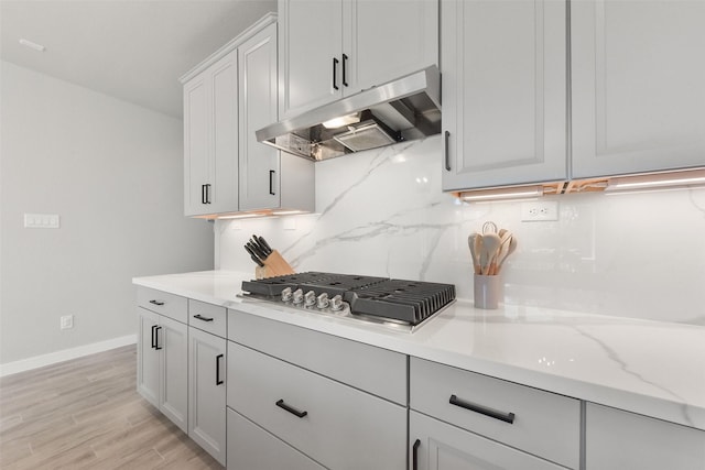 5107 Shimmering Brook Ln, Fulshear, TX 77441 - kitchen with under cabinet range hood, baseboards, decorative backsplash, stainless steel gas cooktop, and light wood finished floors