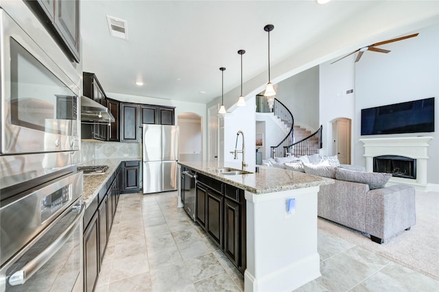 1103 River Delta Ln, Rosenberg, TX 77469 - kitchen with appliances with stainless steel finishes, arched walkways, a sink, light stone countertops, and a fireplace with raised hearth