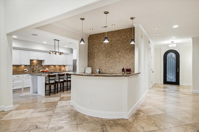 3224 Alabama Ct, Houston, TX 77027 - kitchen featuring decorative backsplash, white cabinetry, dark stone counters, a kitchen bar, and crown molding