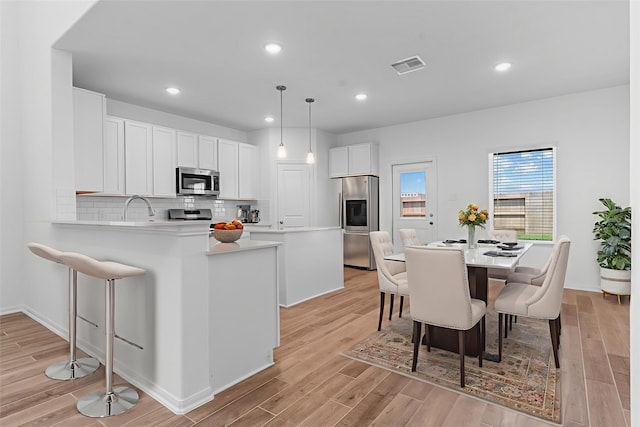 9022 Gull Cyn, Downs, Baytown, TX 77521 - kitchen with appliances with stainless steel finishes, backsplash, light wood-type flooring, a kitchen bar, and light countertops