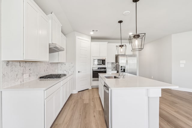 2010 Bluff Oak Ct, Conroe, TX 77304 - kitchen with stainless steel appliances, a sink, light wood finished floors, under cabinet range hood, and backsplash