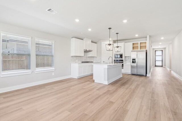 2010 Bluff Oak Ct, Conroe, TX 77304 - kitchen with appliances with stainless steel finishes, light countertops, a kitchen island with sink, backsplash, and light wood finished floors