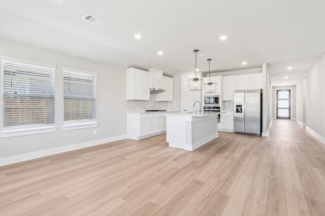 2010 Bluff Oak Ct, Conroe, TX 77304 - kitchen with appliances with stainless steel finishes, light countertops, decorative backsplash, a center island with sink, and light wood-style floors