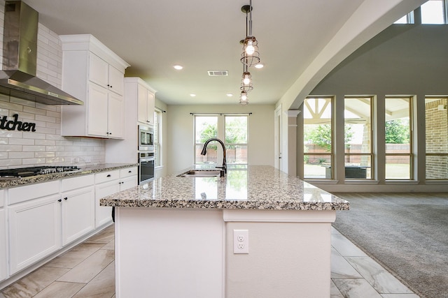 23402 Skylark Falls Trl, Katy, TX 77493 - kitchen with wall chimney exhaust hood, stainless steel appliances, a sink, arched walkways, and light stone countertops