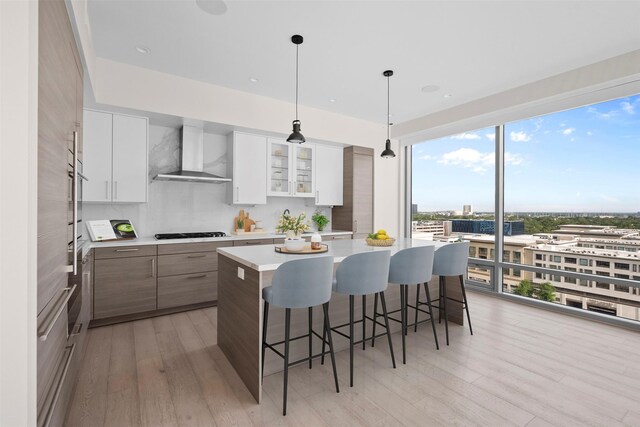 2047 Westcreek Ln Unit 1105, Houston, TX 77027 - kitchen featuring wall chimney range hood, black gas cooktop, light countertops, a kitchen breakfast bar, and light wood finished floors
