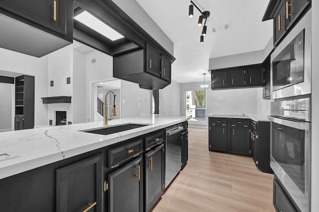 20006 18th Fairway Dr, Humble, TX 77346 - kitchen featuring stainless steel appliances, a sink, light wood finished floors, dark cabinets, and light stone countertops