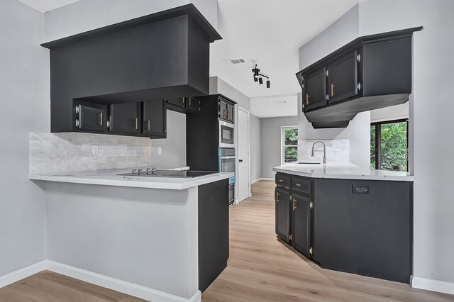 20006 18th Fairway Dr, Humble, TX 77346 - kitchen featuring dark cabinets, light countertops, black electric cooktop, a sink, and backsplash