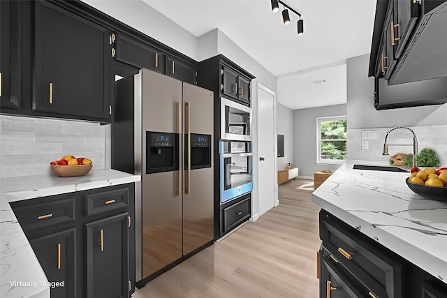 20006 18th Fairway Dr, Humble, TX 77346 - kitchen with stainless steel appliances, dark cabinets, a sink, light wood-style floors, and tasteful backsplash