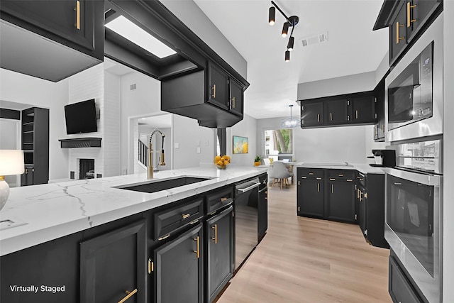 20006 18th Fairway Dr, Humble, TX 77346 - kitchen with appliances with stainless steel finishes, a sink, dark cabinets, light wood finished floors, and light stone counters