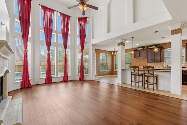 9431 Copper Cove Ln, Rosharon, TX 77583 - unfurnished living room with a fireplace, ceiling fan, light wood-type flooring, a towering ceiling, and decorative columns