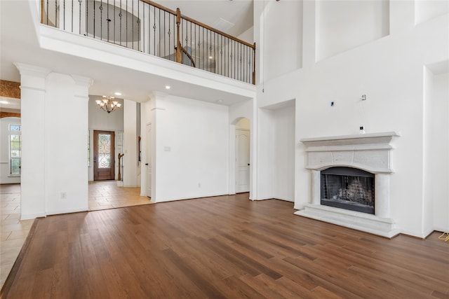 9431 Copper Cove Ln, Rosharon, TX 77583 - unfurnished living room featuring arched walkways, wood finished floors, a chandelier, a fireplace with raised hearth, and a towering ceiling