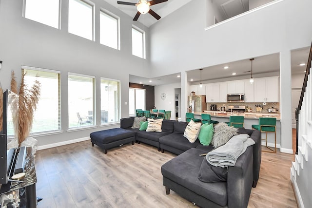 8219 Oxbow Manor Ln, Cypress, TX 77433 - living area featuring a ceiling fan, light wood-style floors, a towering ceiling, and baseboards