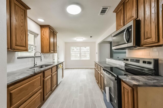 9096 N Comanche Cir, Willis, TX 77378 - kitchen featuring appliances with stainless steel finishes, a sink, brown cabinetry, baseboards, and tasteful backsplash